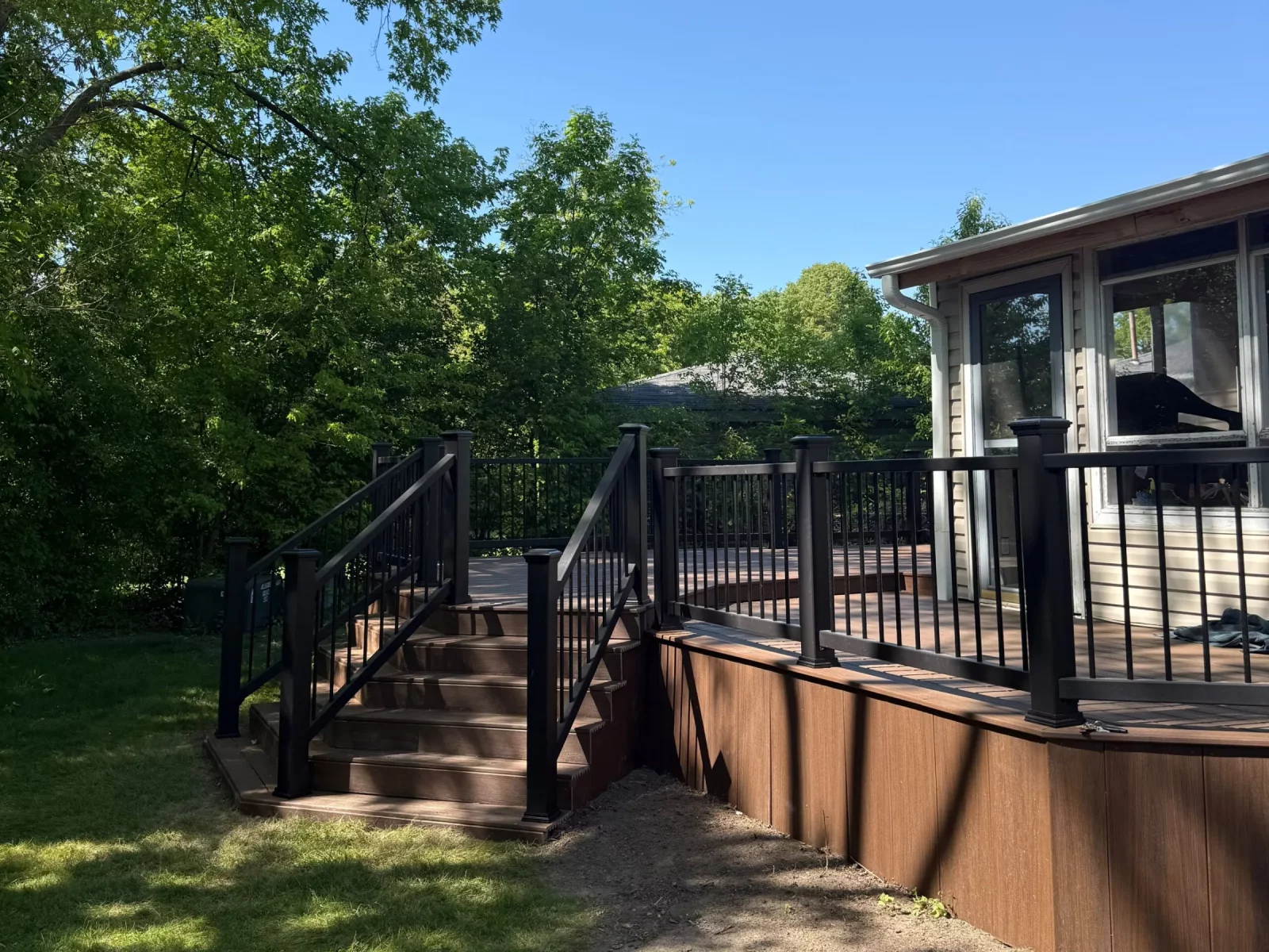 Finished composite deck with black composite railing, black posts, and new stairs under a clear blue sky in Aurora, IL