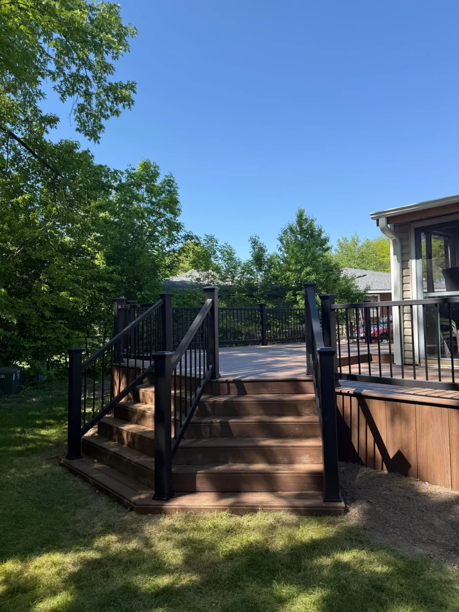 Finished composite deck with black composite railing, black posts, and wide stairs leading to a green lawn in Aurora, IL