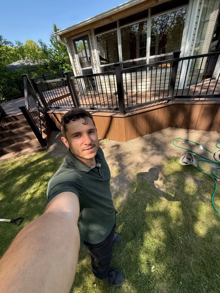 Contractor standing in front of a finished composite deck with black composite railing and brown skirting on a sunny day in Aurora, IL