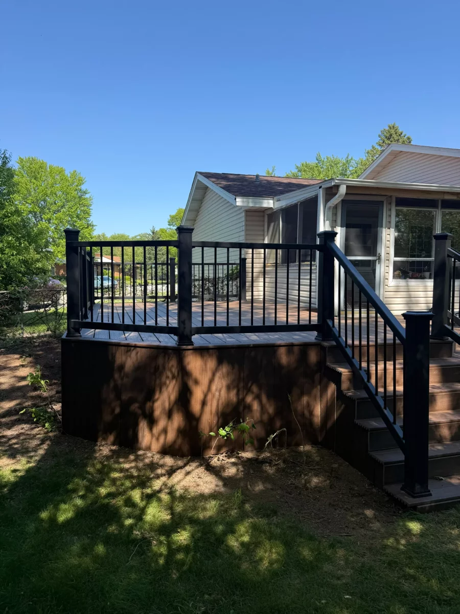 Angled view of a remodeled deck with black composite railing, composite stairs, and matching skirting beside the home in Aurora, IL
